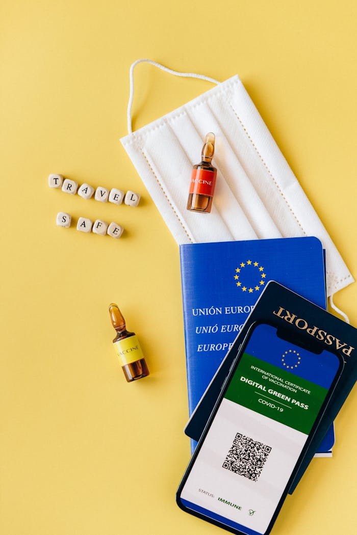 Flat lay of travel essentials including passport, mask, vaccine vials, and digital green pass.
